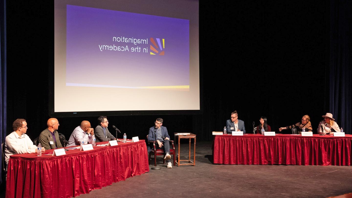 8 faculty and students sit on stage with the moderator, with "Pathways Ignited" displaying in the background