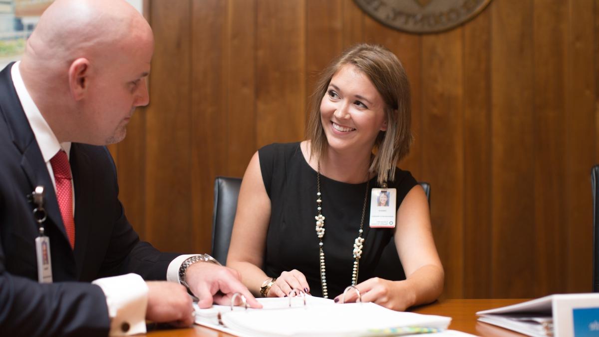 Two executive HCAD students sit at a wooden desk discussing paperwork